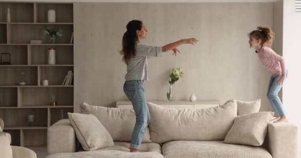 Веселая мама и маленькая дочь прыгают на диване — стоковое видео