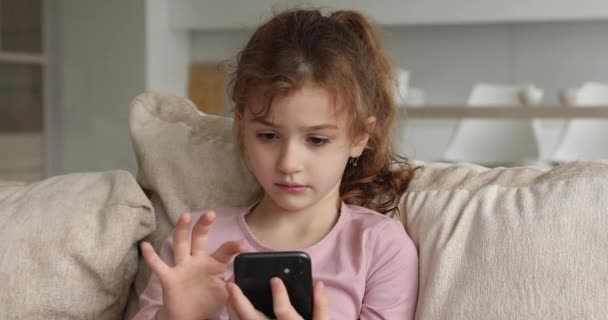 Hübsches 6s kleines Mädchen sitzt auf Sofa mit Smartphone-Gerät — Stockvideo