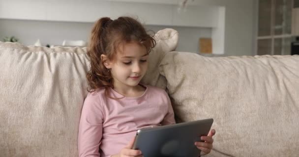 Маленька дівчинка розслабляється на дивані з бездротовим планшетним пристроєм — стокове відео