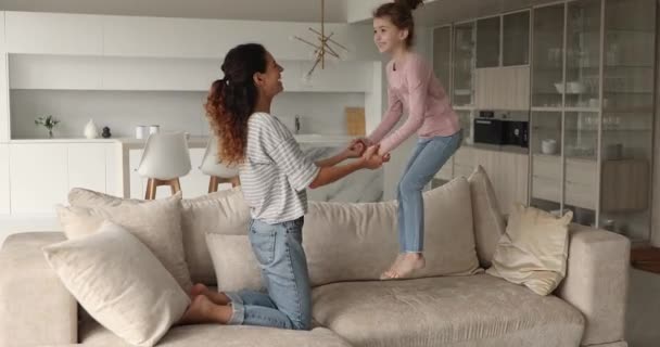 Mamma håller hand med dottern medan hon hoppar på soffan — Stockvideo