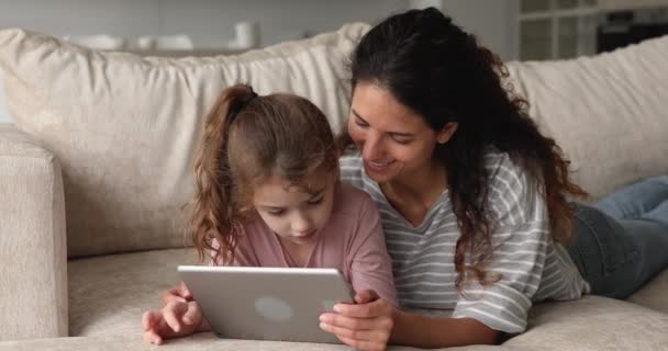 Mujer e hija usando un dispositivo de tableta mientras yacen en el sofá — Vídeo de stock