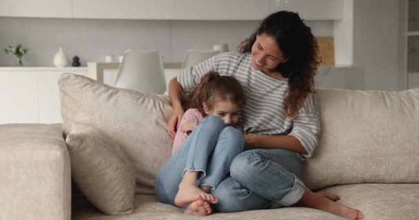 Joven madre cosquillas hija mientras se relajan juntos en cómodo sofá — Vídeos de Stock