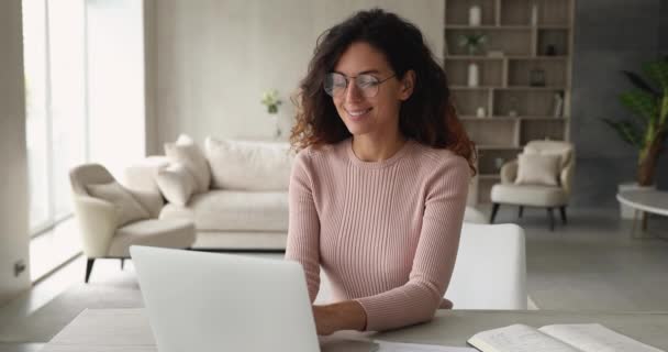 Привлекательная женщина думает, что работает на ноутбуке, сидя за столом в помещении — стоковое видео
