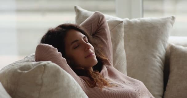 Atraente jovem do sexo feminino relaxante dentro de casa apoiado em almofadas de sofá — Vídeo de Stock