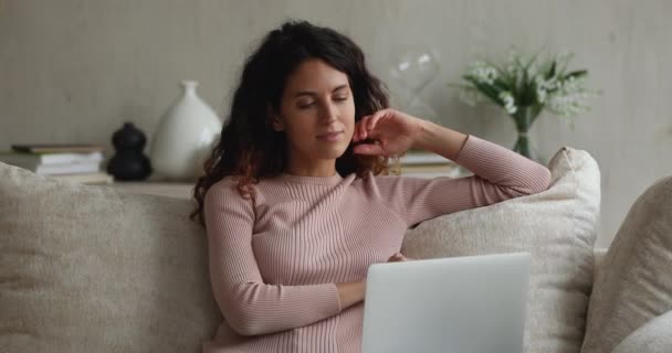 Ελκυστική σκεπτική γυναίκα κάθεται στον καναπέ και εργάζεται σε φορητό υπολογιστή — Αρχείο Βίντεο