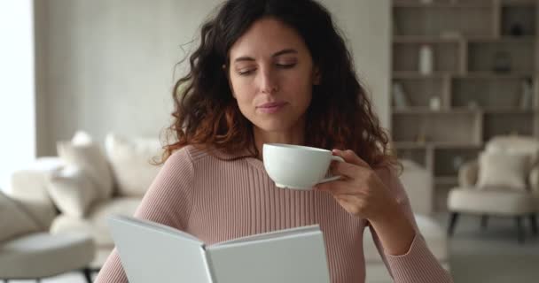 Ειρηνική γυναίκα κάθεται στο σαλόνι διαβάζοντας το βιβλίο πίνοντας τσάι — Αρχείο Βίντεο