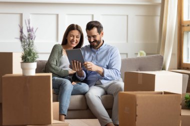 Mutlu çift, taşınma gününde tablet kullanarak kanepede dinleniyor.