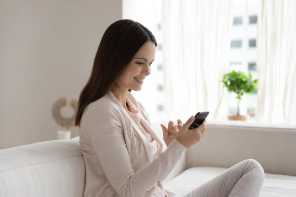 Heureuse jeune femme millénaire avec smartphone relaxant sur le canapé — Photo