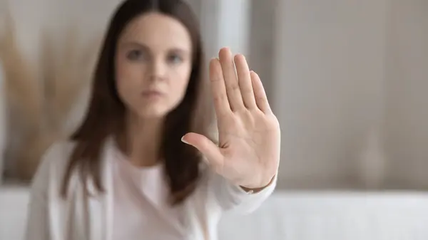 Serious young millennial woman making hand stop gesture at home