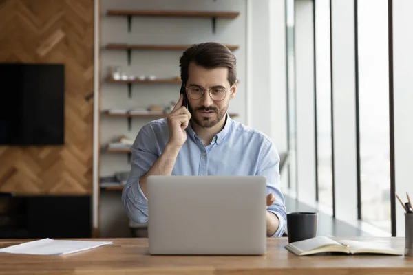 Giovane dipendente di sesso maschile lavorare sul computer parlare sul cellulare — Foto Stock