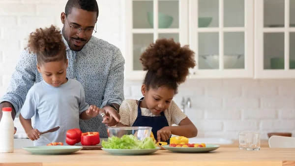 Mutlu Afrikalı Amerikalı kardeş çocuklar babaya yemek hazırlamada yardım ediyor. — Stok fotoğraf