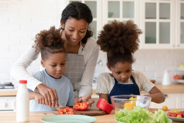 Glückliche Mutter bringt zwei Vorschulkindern vegetarische Mahlzeit bei — Stockfoto