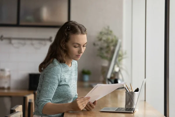 Ung kvinnlig anställd arbetar med dokument med bärbar dator — Stockfoto