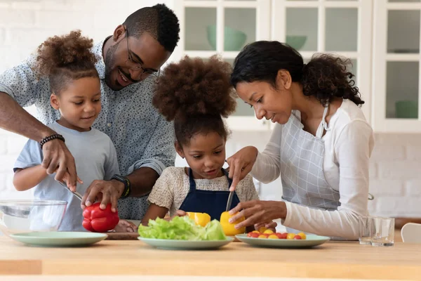 Pareja de familia feliz enseñando a dos niños en edad preescolar a preparar ensalada —  Fotos de Stock