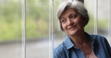 Mutlu, huzurlu, yaşlı kadın pencereden dışarı bakıyor..