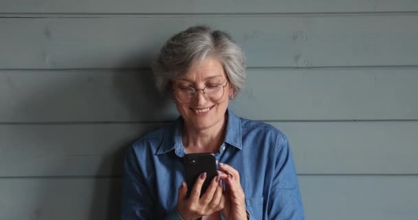 Glückliche ältere reife Frau mit Smartphone, isoliert auf Studiohintergrund. — Stockvideo