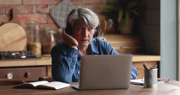 Skupiona kobieta w średnim wieku w słuchawkach, trzymająca połączenie wideo. — Wideo stockowe