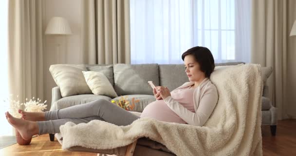 Zwangere vrouw ontspannen alleen op fauteuil met smartphone — Stockvideo