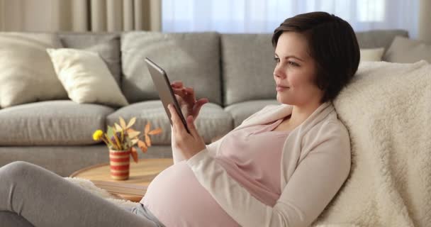 Jonge zwangere vrouw rustend op gezellige fauteuil met digitale tablet — Stockvideo