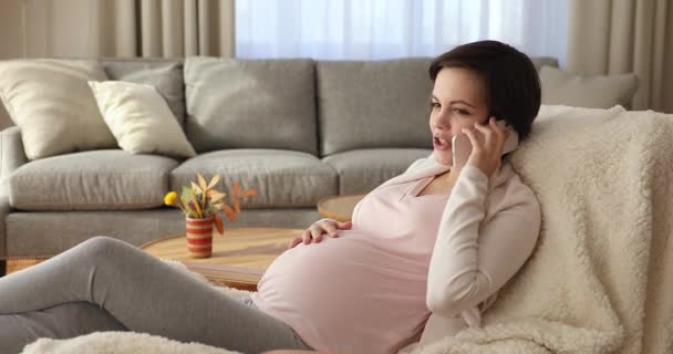 Fiatal terhes nő pihen a karosszéken és telefonál. — Stock videók