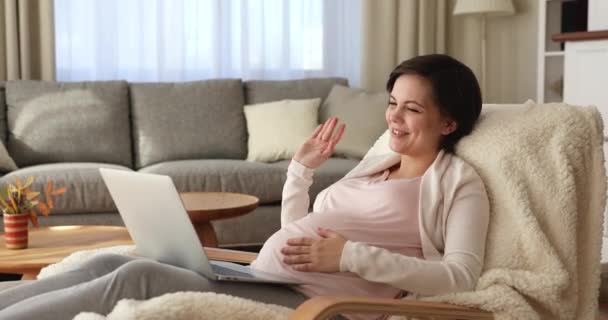 Беременная женщина отдыхает на кресле говорить на видеоконференции с семьей — стоковое видео
