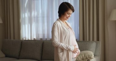 Karnında el ele tutuşan hamile kadın gülümse ve kameraya bak.