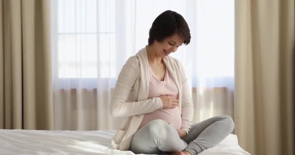 Беззаботная беременная женщина сидит на кровати инсульт большой живот — стоковое видео