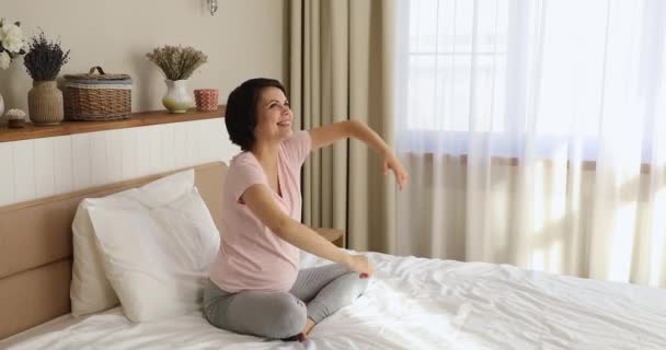 Terhes nő üdvözli az új napot ülni az ágyon a hálószobában — Stock videók