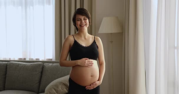Беременная женщина положила руки на голый живот, позируя в помещении — стоковое видео