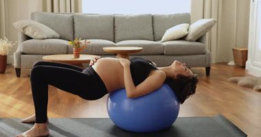 Genç hamile kadın denge topuyla doğum öncesi yoga hareketi yapıyor.