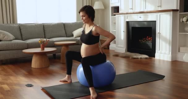Молодая беременная женщина сидит на родовом мяче и занимается пренатальной йогой — стоковое видео