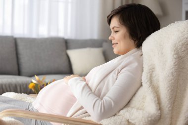 Mutlu hamile kadın, evinde sandalyede rahatla.