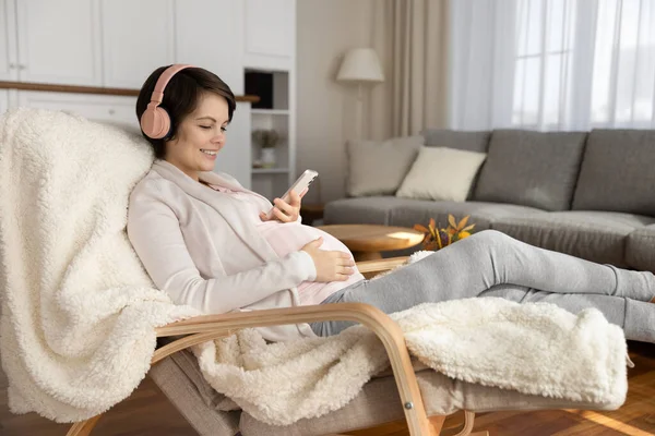 Šťastná těhotná žena ve sluchátkách pomocí smartphonu — Stock fotografie