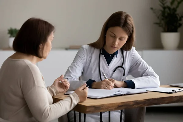 Женщины-врачи отмечают жалобы взрослых пациентов в дневнике — стоковое фото