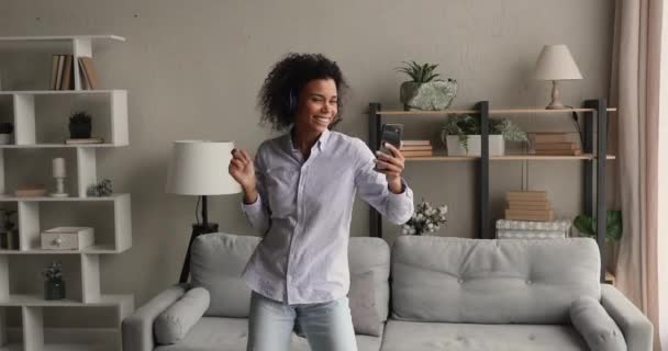 Afrikaanse vrouw holding smartphone luistert naar muziek door middel van koptelefoon dansen — Stockvideo
