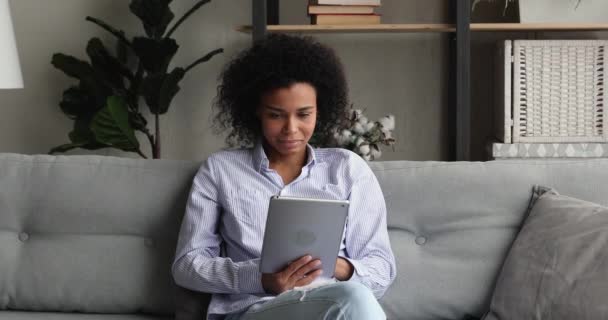 Jovem mulher africana sente-se no sofá descansando usando tablet digital — Vídeo de Stock