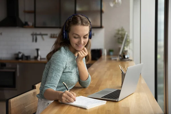 헤드폰을 끼고 멀리 노트북으로 연구하는 암컷의 미소짓기 — 스톡 사진