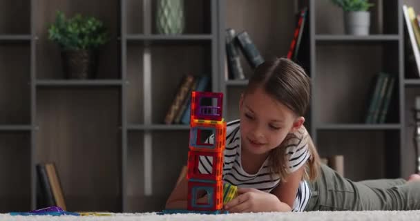 Милая маленькая девочка лежит на полу играть творческий магнитный конструктор — стоковое видео