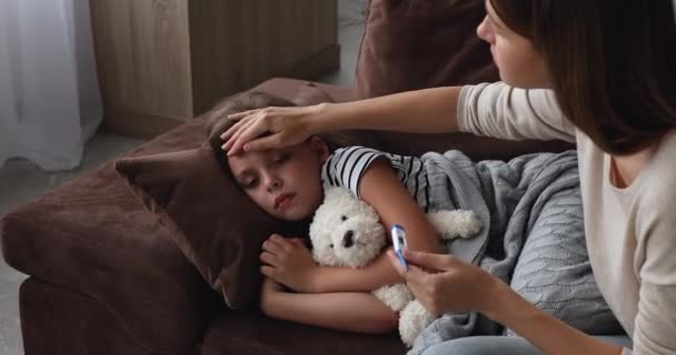 Madre comprobar la temperatura de cuidado de la hija enferma acostada en el sofá — Vídeo de stock