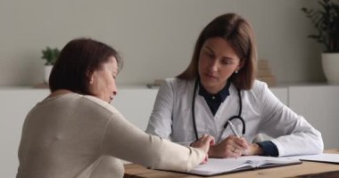 Yaşlı hastanın şikayetlerini ve sağlık sorunlarını not eden kadın doktor