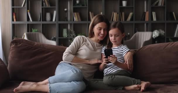 Liebevolle Mutter und kleine Tochter sitzen auf Sofa mit Smartphone — Stockvideo