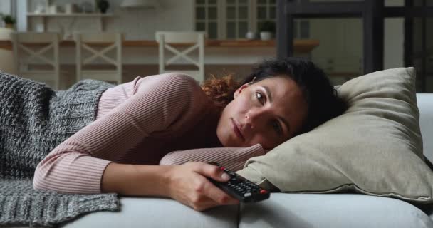 Ленивая молодая женщина лежит на диване на домашнем переключателе каналов — стоковое видео