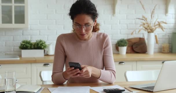 Kadın hesaplamalar yapar, faturaları akıllı telefondaki banka uygulaması ile öder. — Stok video