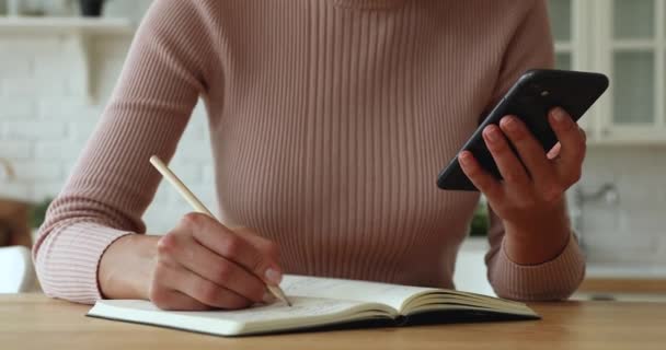 Vrouw schrijft informatie genomen van internet in notebook — Stockvideo