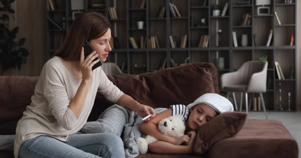 Madre hablar por teléfono celebración termómetro comprobar la temperatura de la hija — Vídeo de stock