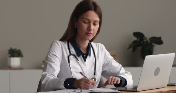 Médico sentado en el lugar de trabajo trabajando en portátil llenar diario médico — Vídeo de stock