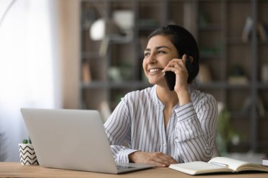 Gülümseyen Hintli kadın telefonda konuşuyor, çalışma masasında oturuyor.