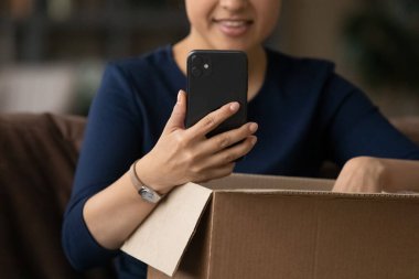 Close up Indian woman using smartphone and unpacking parcel clipart
