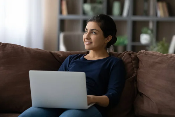 Smiling dreamy Indian woman distracted from laptop, looking to aside — Stock Photo, Image