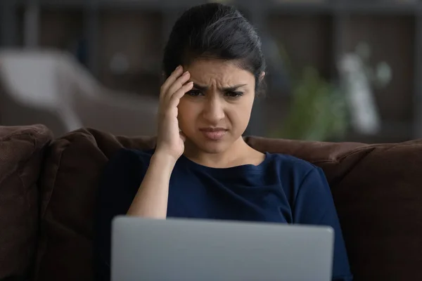 Close up unhappy Indian woman looking at laptop screen